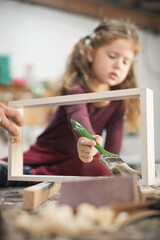 Father and daughther painting wooden frame in workshop