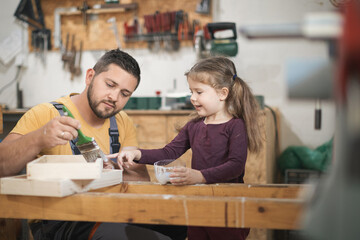 Father and daughther painting wooden frame in workshop