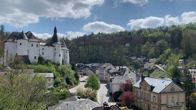 Panoramic, scenic view of Clervaux Castle (Chateau) and Clervaux town houses. People are walking at city centre. Motion of car. Clervaux, Luxembourg