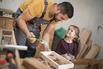 Father and daughther painting wooden frame in workshop