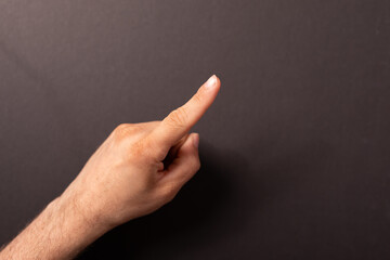 Close-up of a hand with index finger pointing upwards against a dark backdrop. Ideal for concepts...