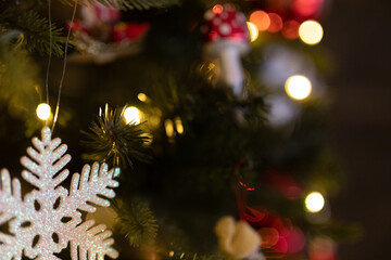 Close-up of a glittering snowflake ornament hanging on a decorated Christmas tree with warm lights.