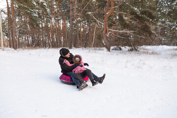 Father and daughter having fun with snow tube in the forest