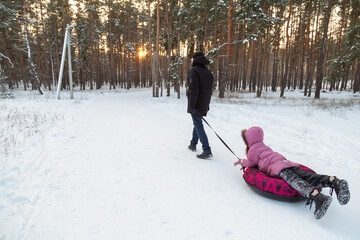 Father and daughter having fun with snow tube in the forest