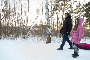 Dad with his daughter walking with snow tubing in the winter forest