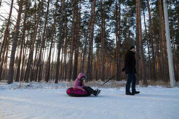 Dad takes his daughter on a snow tube in the forest