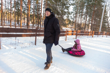 Dad takes his daughter on a snow tube in the forest