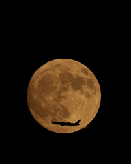 Golden full moon and plane silhouette at dusk, with deep black background