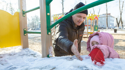 Grandfather playing with his granddaughter on the playground in the park in winter