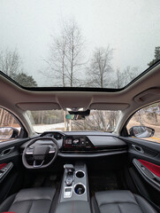The interior view of a car featuring a sunroof and lush trees in the background
