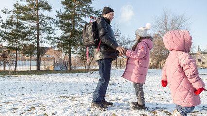 Grandfather walks with his granddaughters after school in the park in sunny winter day