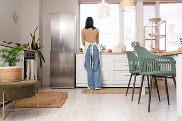 Young woman cooking in stylish kitchen with modern refrigerator, back view