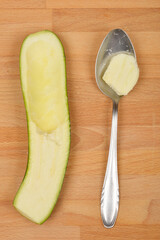 A halved and scooped-out zucchini lies next to a spoonful of its pulp on a wooden surface