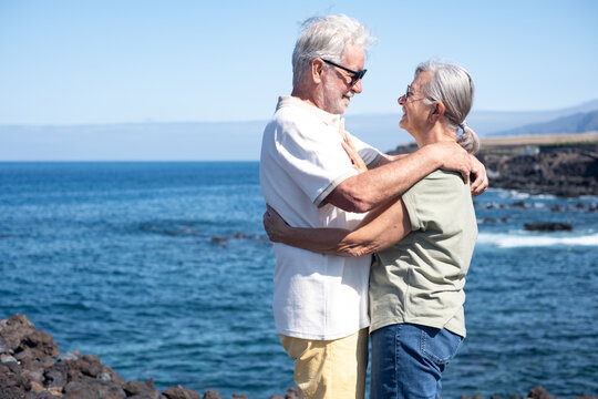 Lovely caucasian senior couple embracing standing on the rocky beach enjoying freedom and vacation in retirement