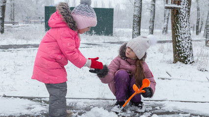 Two little girls in colorful clothes play outdoors during a snowfall.