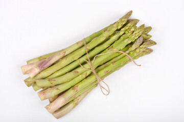 A bundle of fresh green asparagus spears is tied with brown twine and angled on a light gray...