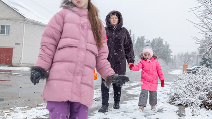 Grandmother and girls walk along a snowy street in winter
