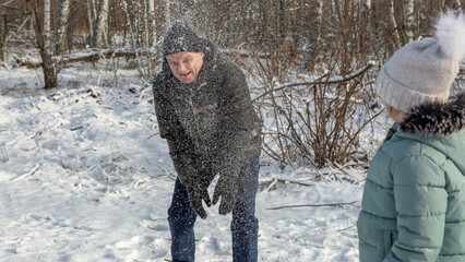 Little girls play with snow with her grandfather in winter forest