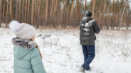 Little girls play with snow with her grandfather in winter forest