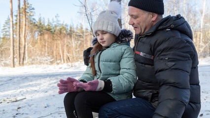 grandfather and granddaughter walk in a snowy forest, have fun together