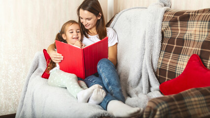 Young mother reading a book to her little daughter at home
