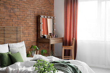 Wooden dressing table and bed near brick wall in interior of bedroom