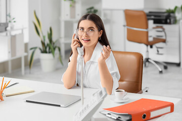 Obraz premium Young secretary talking by telephone at table in office