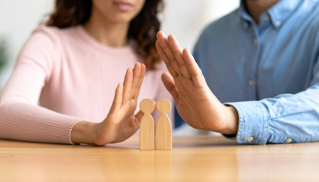 Two people with raised hands blocking and dividing wooden man and woman figures, symbolizing conflict resolution, separation, or relationship boundaries in calm, neutral setting