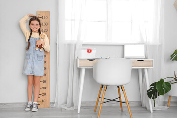Cute girl with toy measuring height near stadiometer in clinic