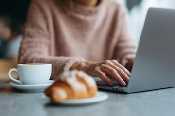 Woman working on laptop in cozy cafe with cup of coffee and croissant, creating relaxed and productive atmosphere for remote work or study