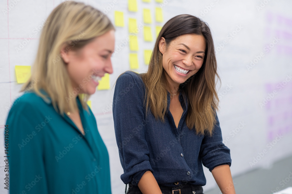 Poster two women smiling in modern office, standing near wall with sticky notes, collaborating on project, 