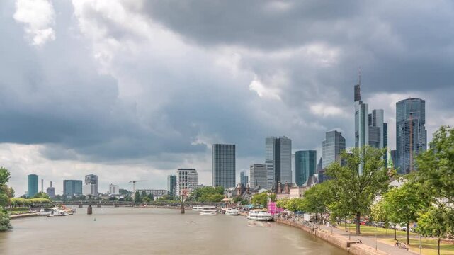 Hyperlapse of the historical Eiserner Steg (Iron Bridge) over the Main River in Frankfurt, Germany. Skyscrapers skyline and waterfront reflect in the water under a cloud-filled sky timelapse