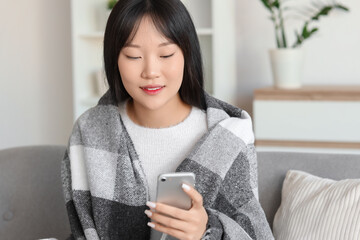 Young Asian woman with soft plaid using mobile phone at home