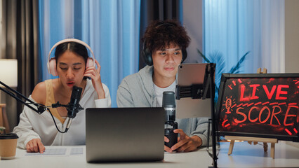 Young happy Asian couple wear headphone sit on desk online live streaming football live score...