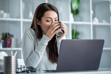 Young woman freezing in cold office, holding warm cup