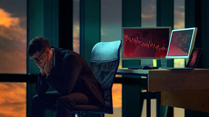 Businessman in suit sitting in office, two computer screens displaying downward trending graphs....