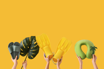 Female hands with beach accessories and palm leaf on yellow background