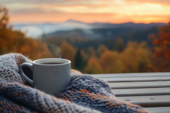 Warm coffee mug resting on a cozy blanket with a serene autumn sunset in the background