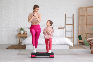 Sporty young mother and her cute little daughter exercising on aerobic stepper at home. Mother Day...