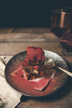 Stack of freshly baked red dusted chocolate brownies on timber surface with dark background