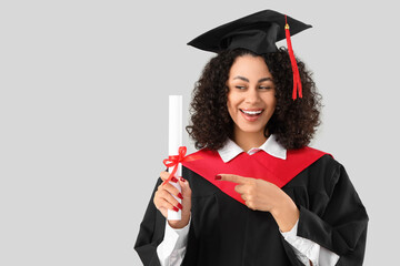 Happy African-American female graduate pointing at diploma on white background