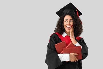 Surprised African-American female graduate with books on white background