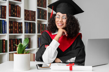 Pretty African-American female graduate with laptop sitting at table in library