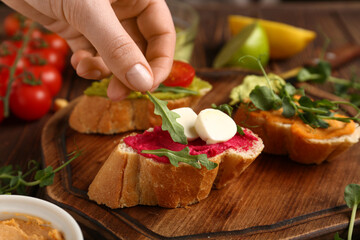 Woman preparing tasty sandwiches with hummus on wooden table, closeup