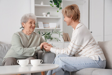 Fototapeta premium Mature woman with her mother holding hands on sofa at home