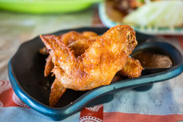 Close-up of crispy fried chicken wings served in a black dish on a decorative table setting.