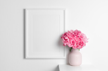 Portrait picture frame mockup on white wall, blank frame with copy space, pink peony flowers decor...