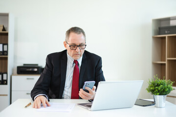 Obraz premium Confident businessman in suit, working on laptop and smartphone at office desk. Professional executive, leadership, strategy
