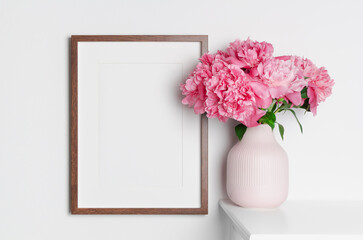 Blank wooden frame mockup on white wall with peony flowers for artwork, picture, photo or poster presentation, blank frame with copy space
