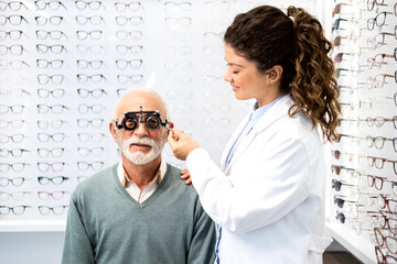 Experienced optometrist checking senior man eyesight focus and diopter using test eyeglasses...